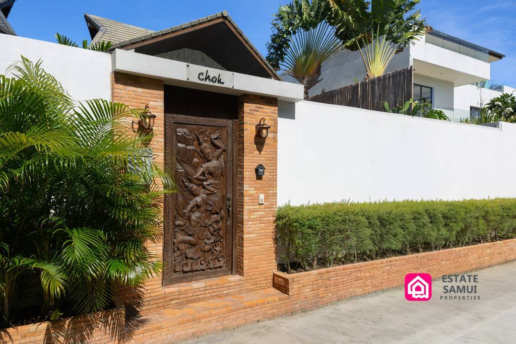 Private villa entrance with carved wooden gate and tropical landscaping