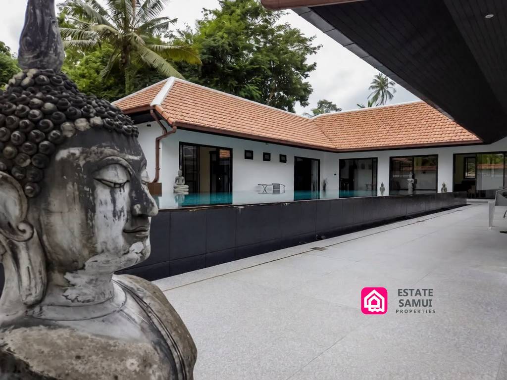 Courtyard swimming pool beside tiled villa buildings and Buddha statue
