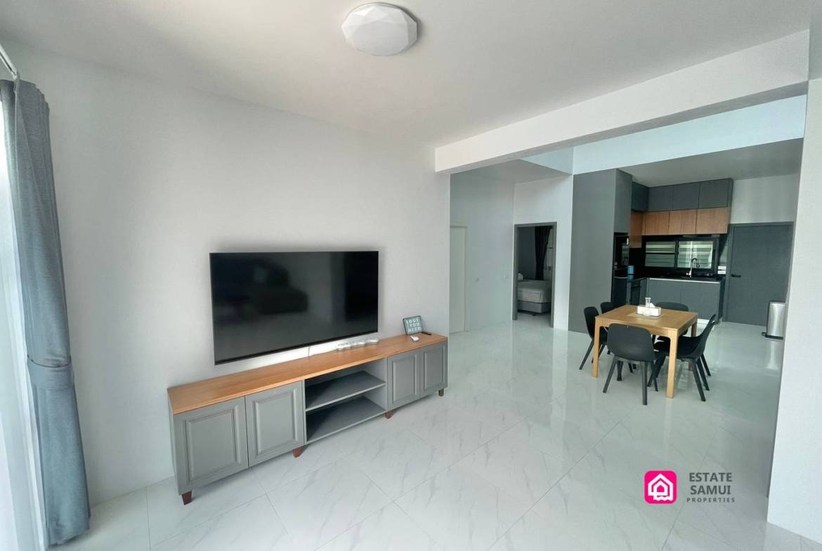 Open-plan living and dining area with television and compact kitchen beyond.