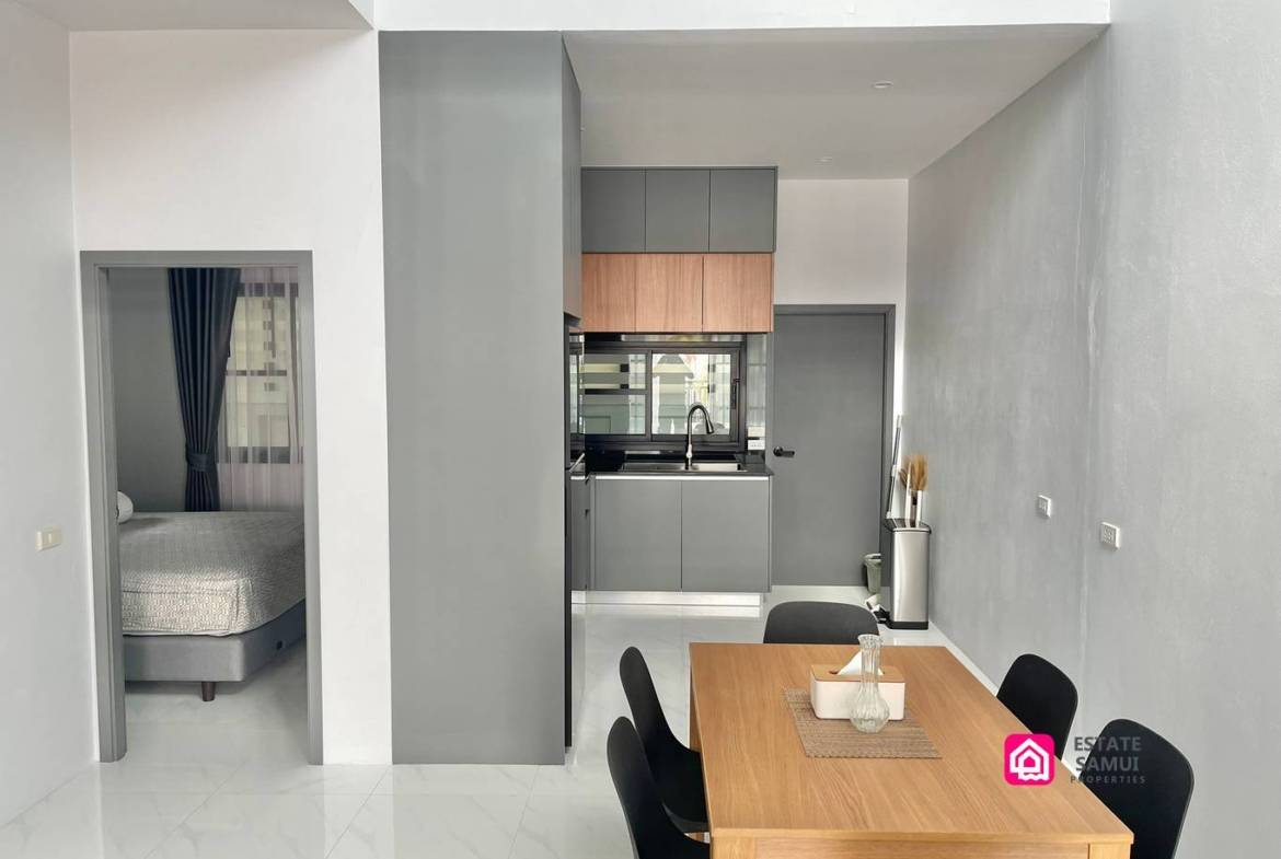Wooden dining table with black chairs beside the kitchen and bedroom doorway.
