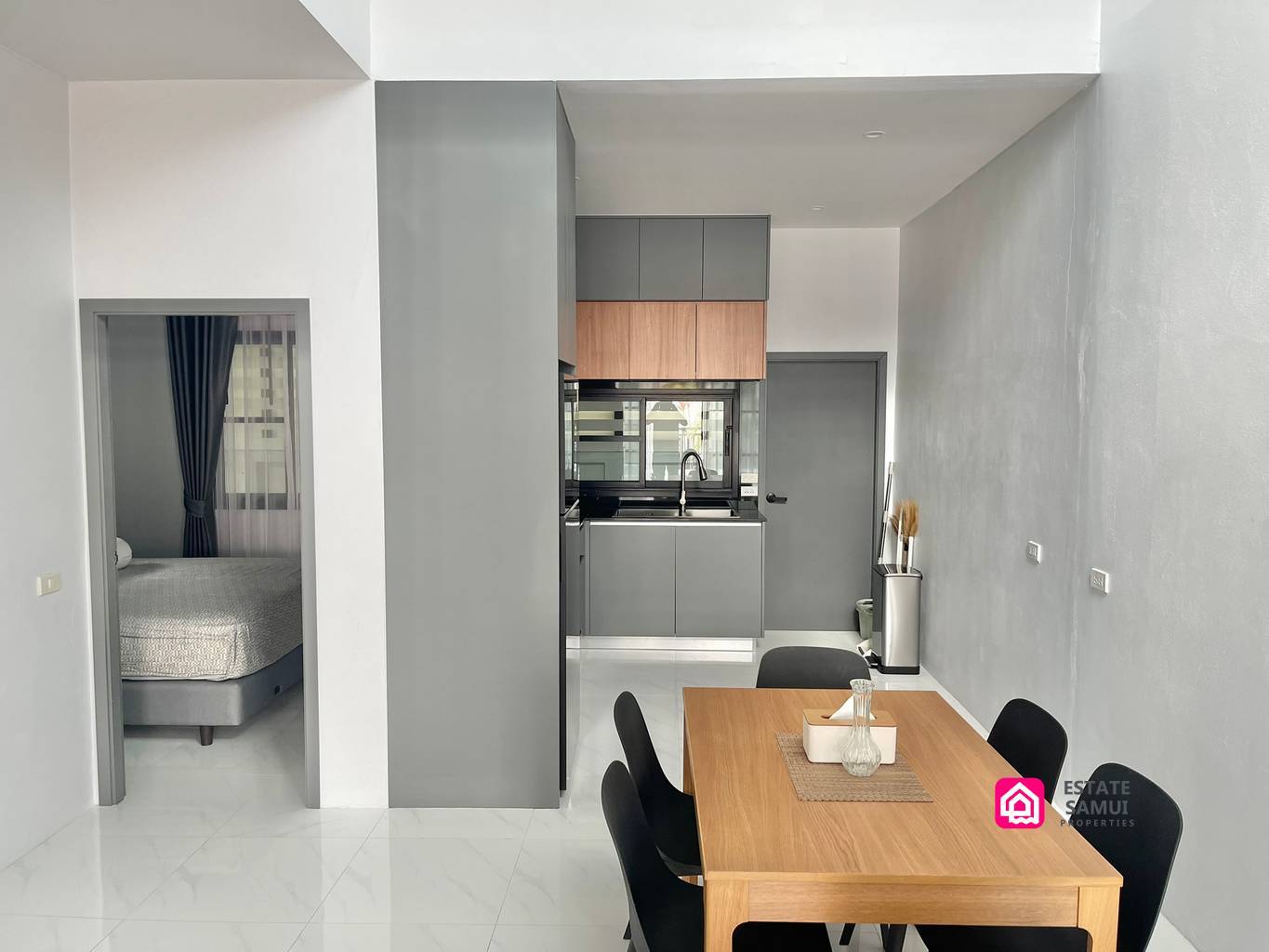 Wooden dining table with black chairs beside the kitchen and bedroom doorway.