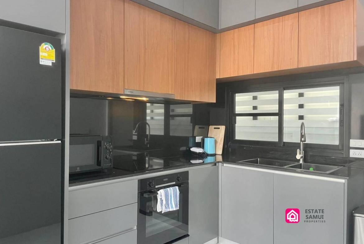 Compact kitchen with built-in oven, hob and wood-effect upper cabinets.