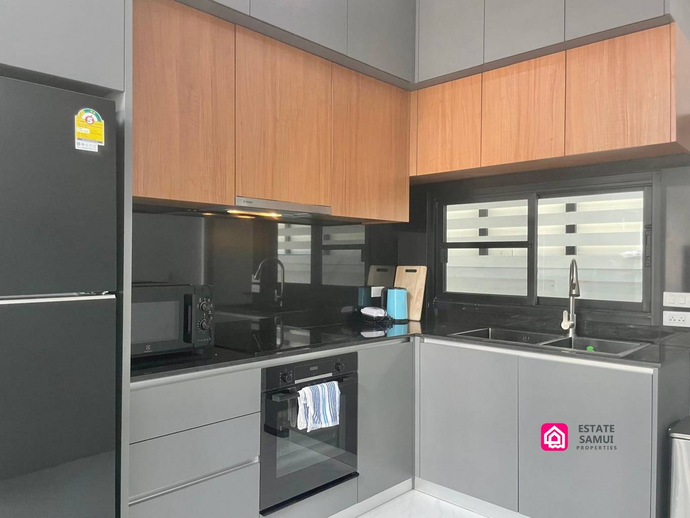 Compact kitchen with built-in oven, hob and wood-effect upper cabinets.