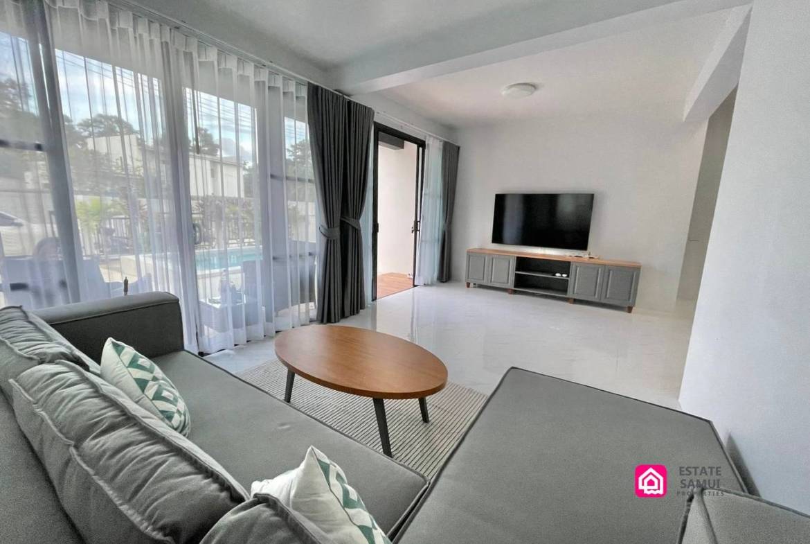 Bright living room with grey corner sofa and pool-facing sliding doors.