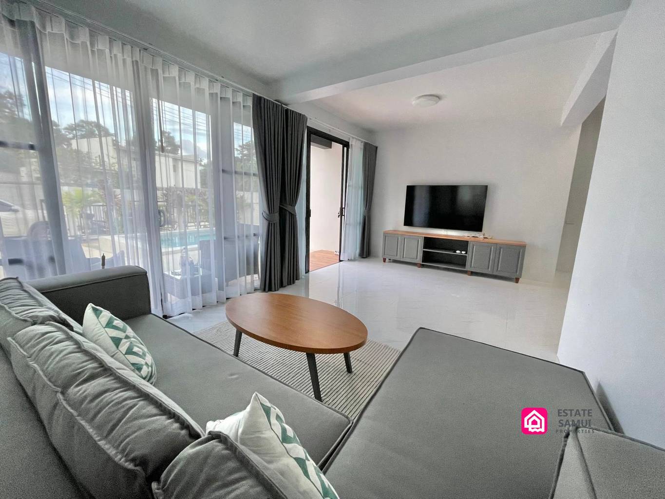Bright living room with grey corner sofa and pool-facing sliding doors.
