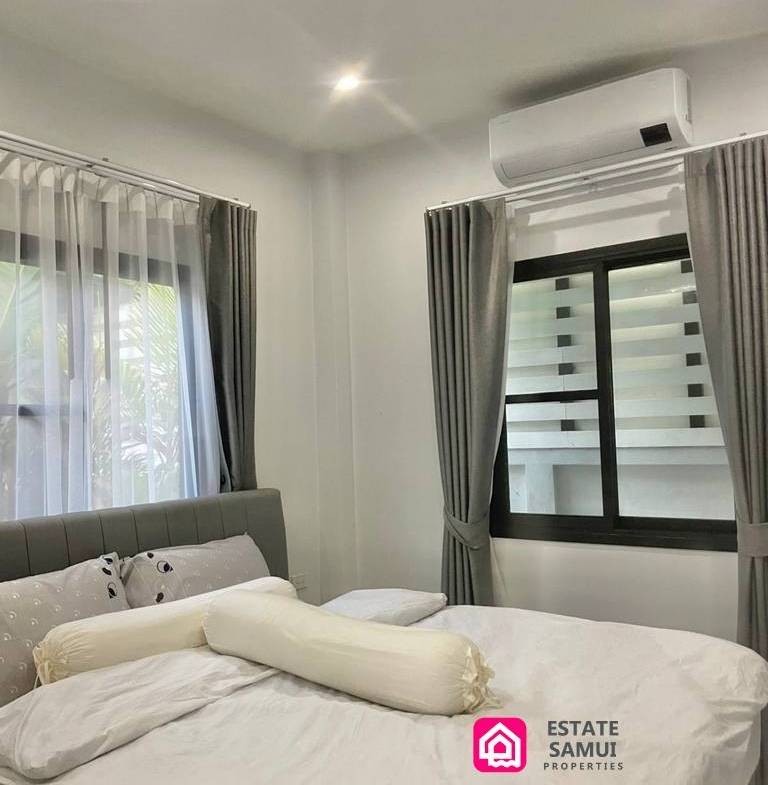 Double bedroom with grey headboard, curtained windows and wall-mounted air conditioning.