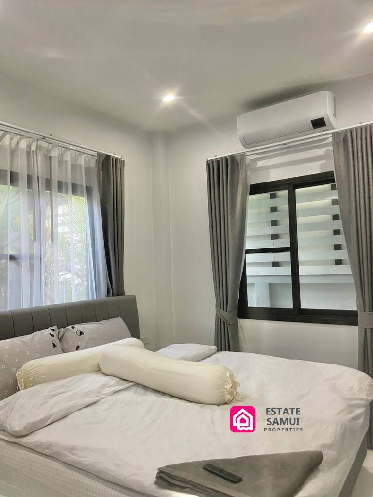 Double bedroom with grey headboard, curtained windows and wall-mounted air conditioning.