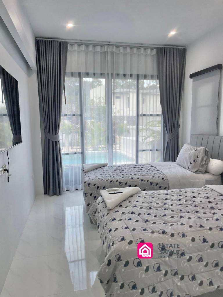 Twin bedroom with wall-mounted television and sliding doors overlooking the pool.
